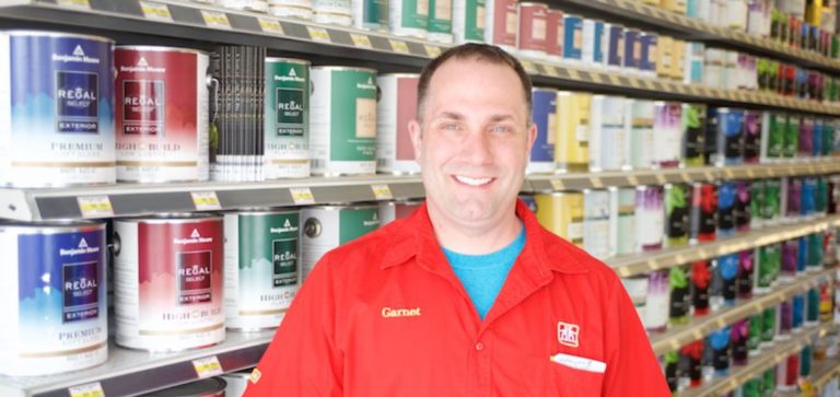 Smiling man in red Home Hardware shirt standing in front of a shelf full of paint cans