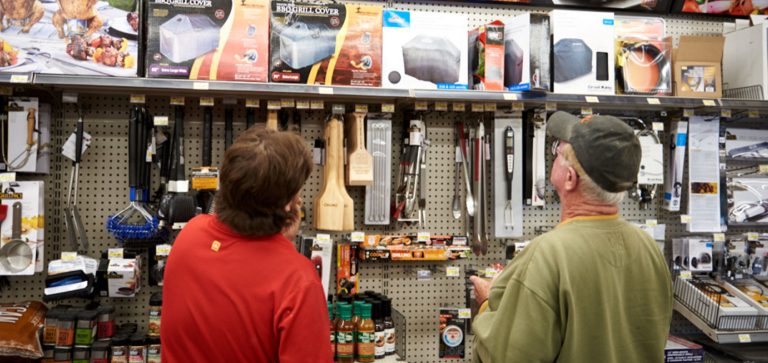Hardware employee in a red shirt and a customer are looking at a wall of bbq tools