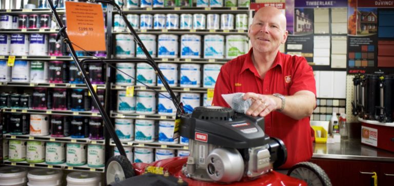 Male employee smiling behind a lawnmower